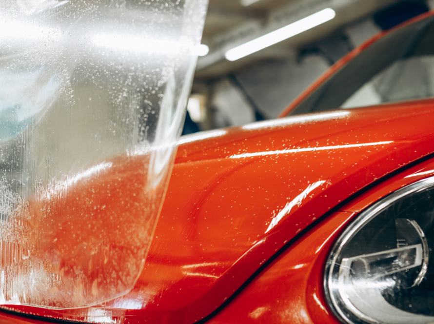 Close-up of a red car being installed with paint protection film at a car detailing studio