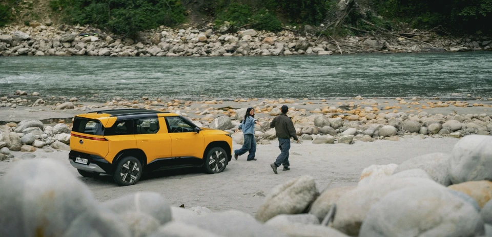 A young couple strolls in front of their Andaman Adventure Tata Sierra in an outdoor, rocky terrain.