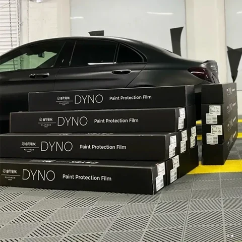 STEK DYNO PPF boxes stacked in front of a black car